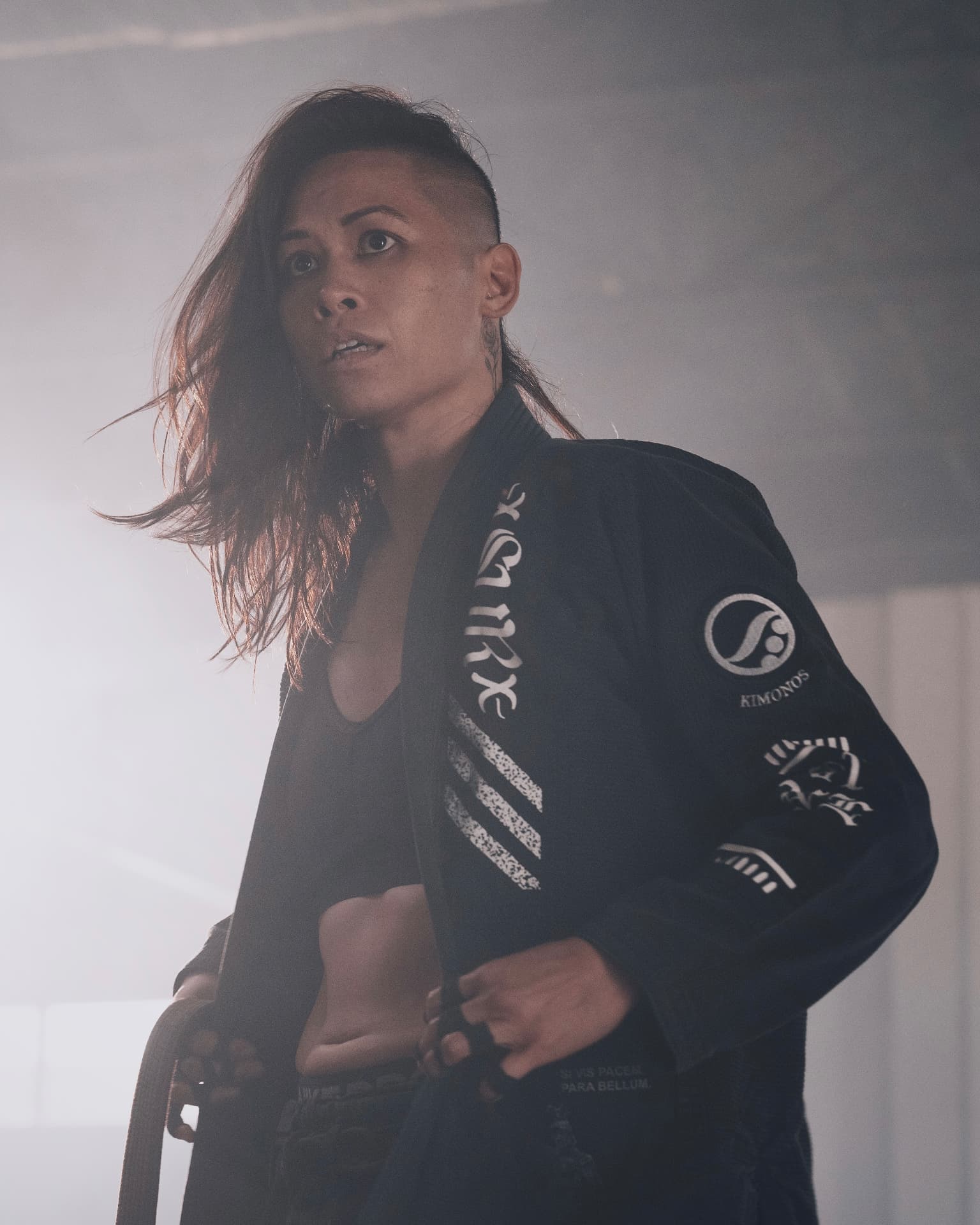 Katty Strite in a black Shoyoroll jiu-jitsu gi, tying her belt in a hazy gym