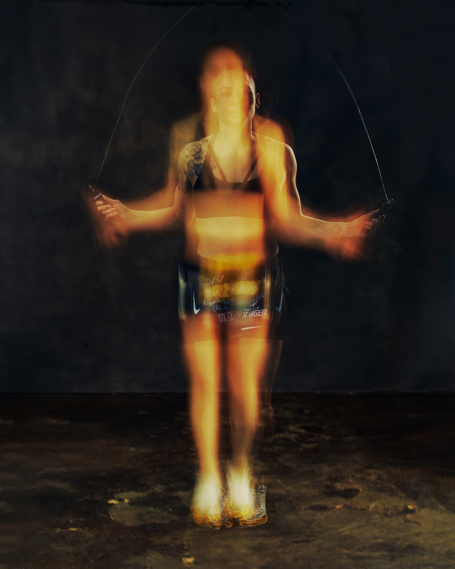 Long-exposure image of Katty Strite skipping rope, her body blurred in warm amber light against a dark wall