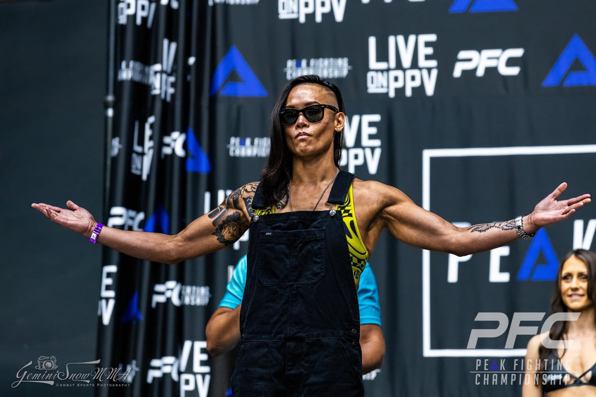 Katty Strite on stage at a Peak Fighting Championship weigh-in, arms outstretched in front of the PFC backdrop