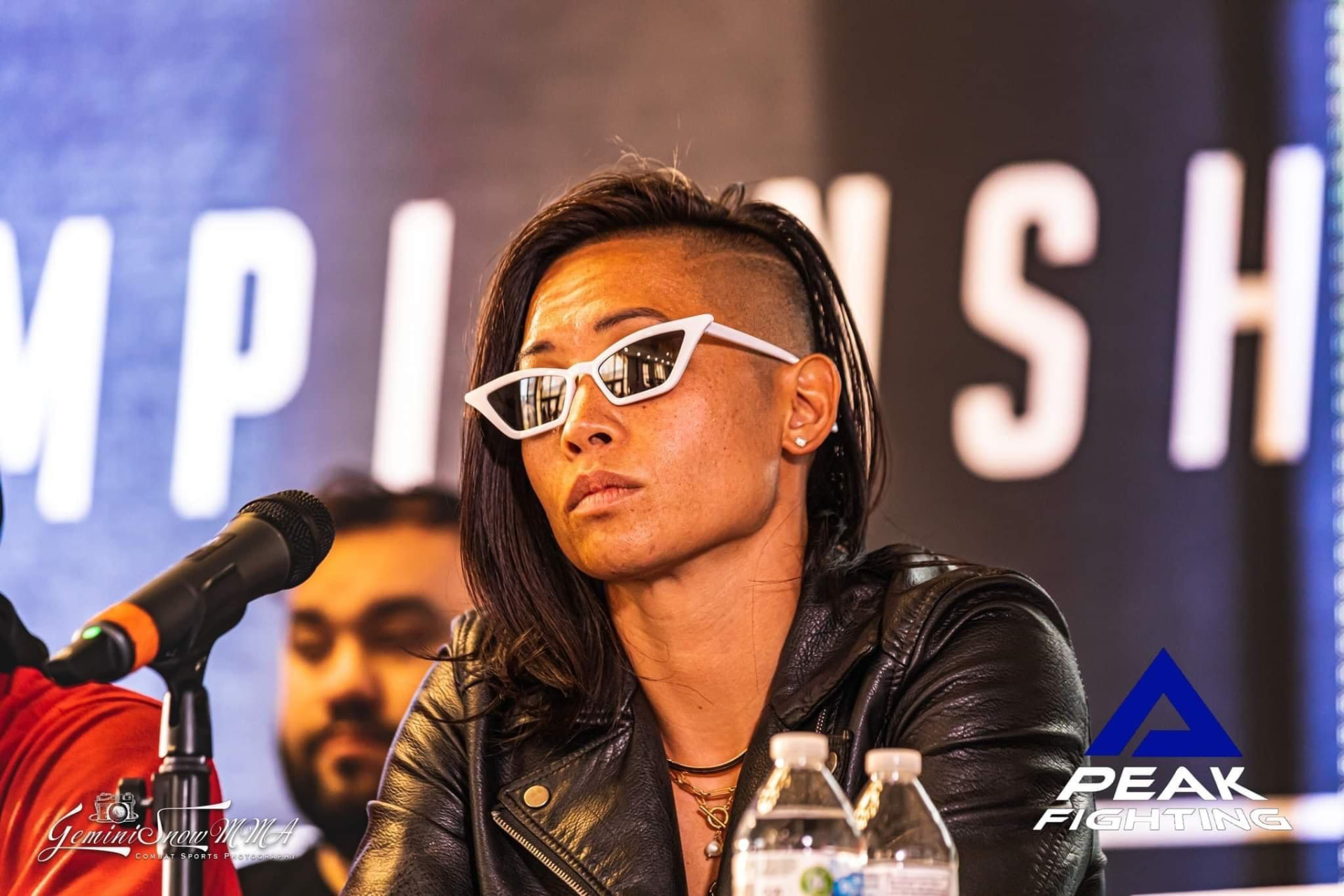Katty Strite at a Peak Fighting Championship press conference in a leather jacket and white sunglasses